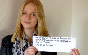 Eine junge Dame hält ein Schild hoch, auf dem steht: Ich bin Davinah. Ich liebe es Volleyball zu spielen und zu lesen. Ich bin die Jüngste in meiner Familie. Und ich bin Mormone. Sie beantwortet die Frage "Gibt es Mormonen in Deutschland?"