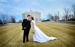 Ein gerade aneinander gesiegeltes Ehepaar küsst sich, im Hintergrund ist ein Tempel der Mormonen zu sehen.