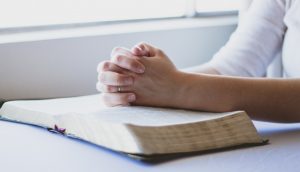 Zu sehen sind zum Beten gefaltete Hände auf einer Bibel.