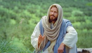 Jesus Christus sitzt auf einer Wiese und scheint mit jemandem zu sprechen.