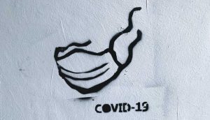 Zu sehen ist ein mit einer Sprühdose gemalte Maske und ein Covid-19-Schriftzug.
