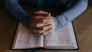 Zu sehen sind wie zum Gebet gefaltene Hände auf einer Bibel.