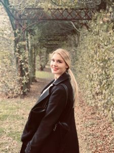 Dies ist ein weiteres privates Foto von Leslie. Sie steht in einem Park und dreht sich lächelnd zur Kamera.