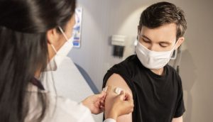 Eine Ärztin klebt ein Pflaster auf den Arm eines zuvor geimpften jungen Mannes.