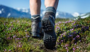 Man sieht die Wanderschuhe und Waden eines Mannes, der in Richtung der Berge unterwegs ist.