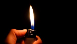 Zu sehen ist eine Hand, die ein Feuerzeug hält. Aus diesem kommt eine Flamme.