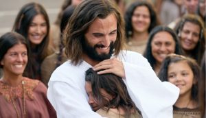 Jesus umarmt ein junges Mädchen und lächelt dabei.
