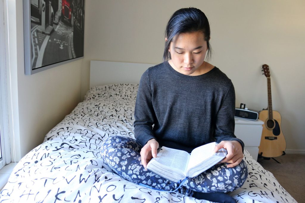 Eine junge Frau sitzt auf dem Bett und studiert heilige Schrift