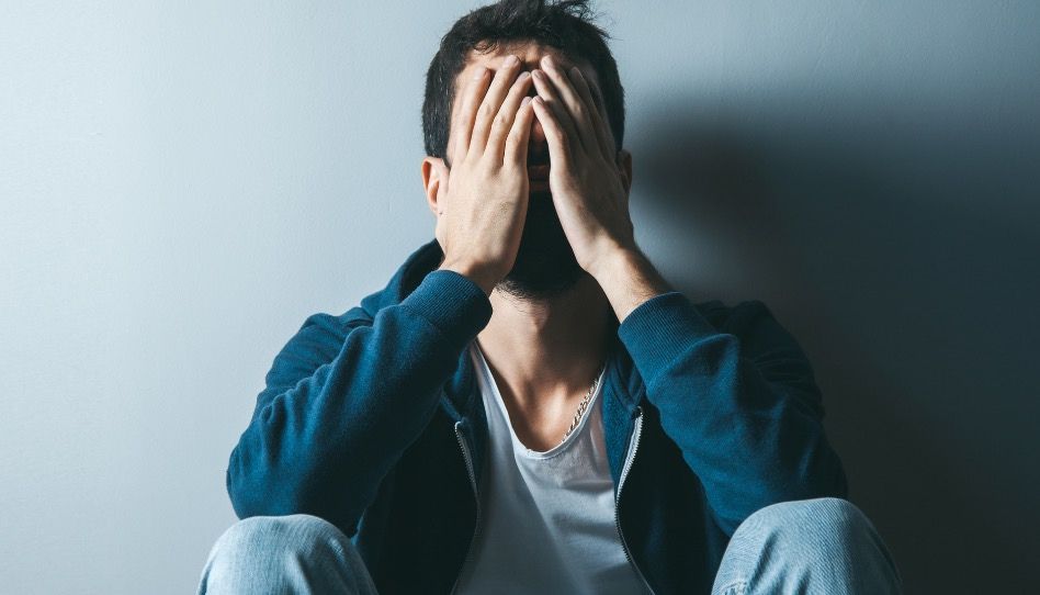 Ein Mann sitzt mit dem Rücken an der Wand und hält sich die Hände vor das Gesicht