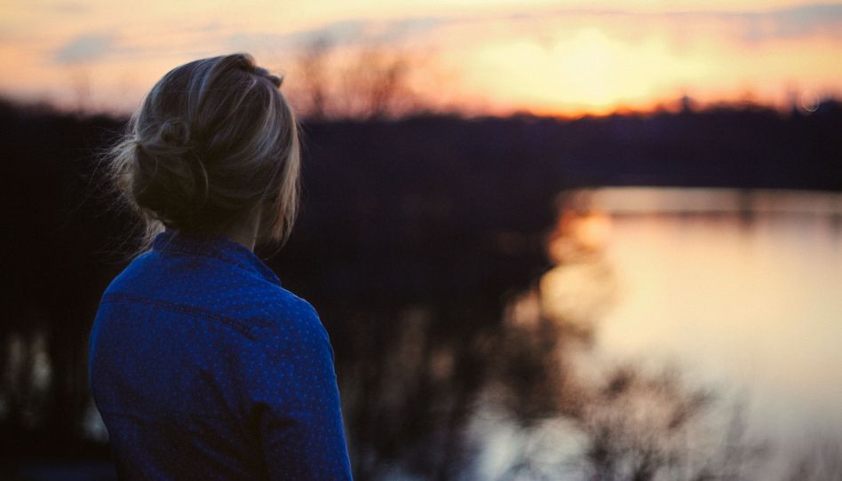 Eine Frau steht am Wasser und schaut sich einen Sonnenuntergang an.