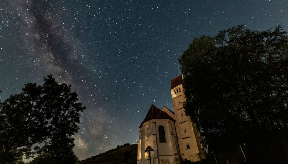 Zu sehen ist ein Sternenhimmel. Auf der unteren rechten Seite ist eine Burg im Vordergrund.