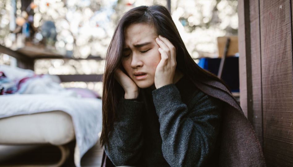 Eine junge Frau sieht verzweifelt aus. Sie hat die Augen geschlossen und ihren Kopf in den Händen.